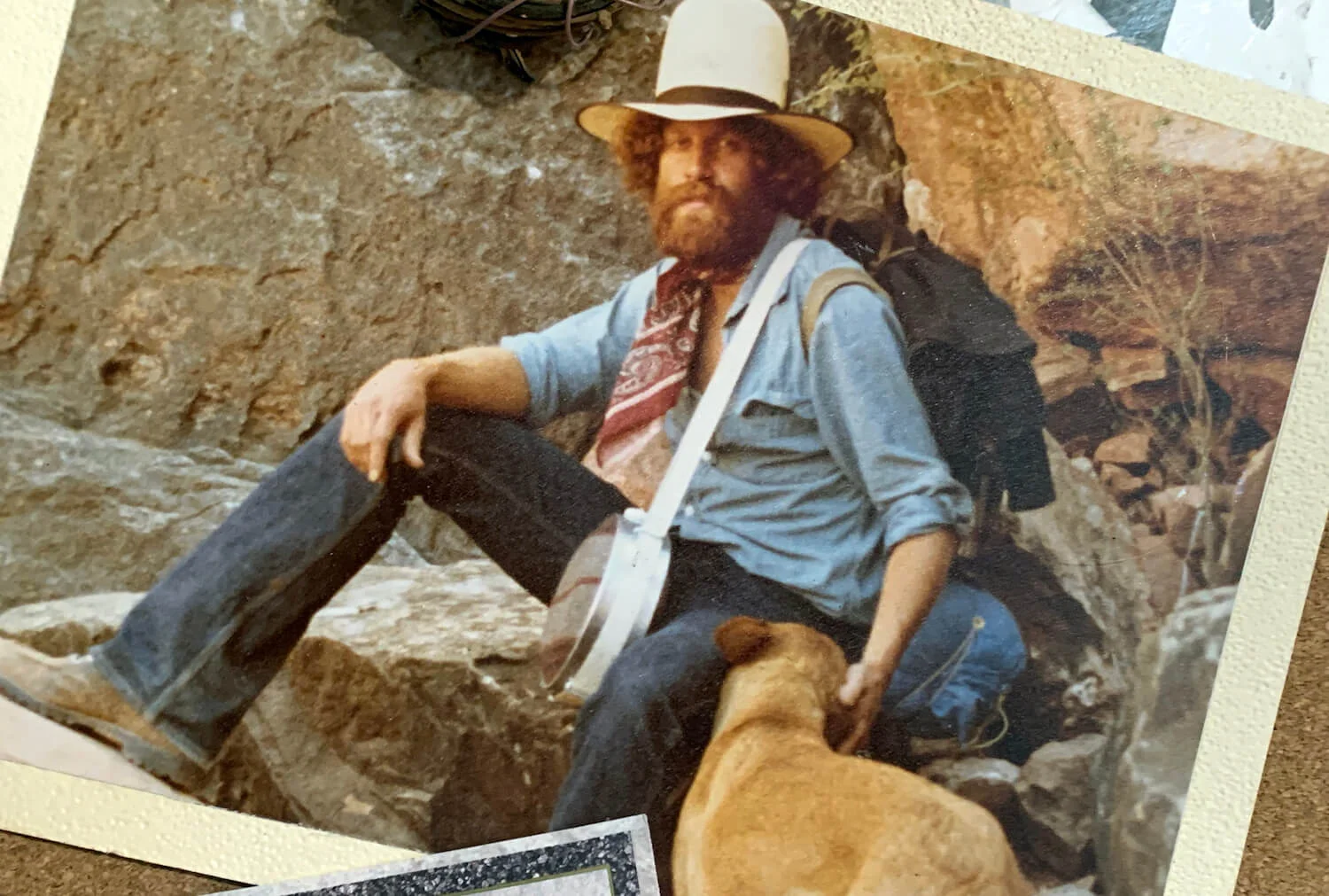 Jerry as a young man, sitting on rocks with a canteen, big hat, and a dog